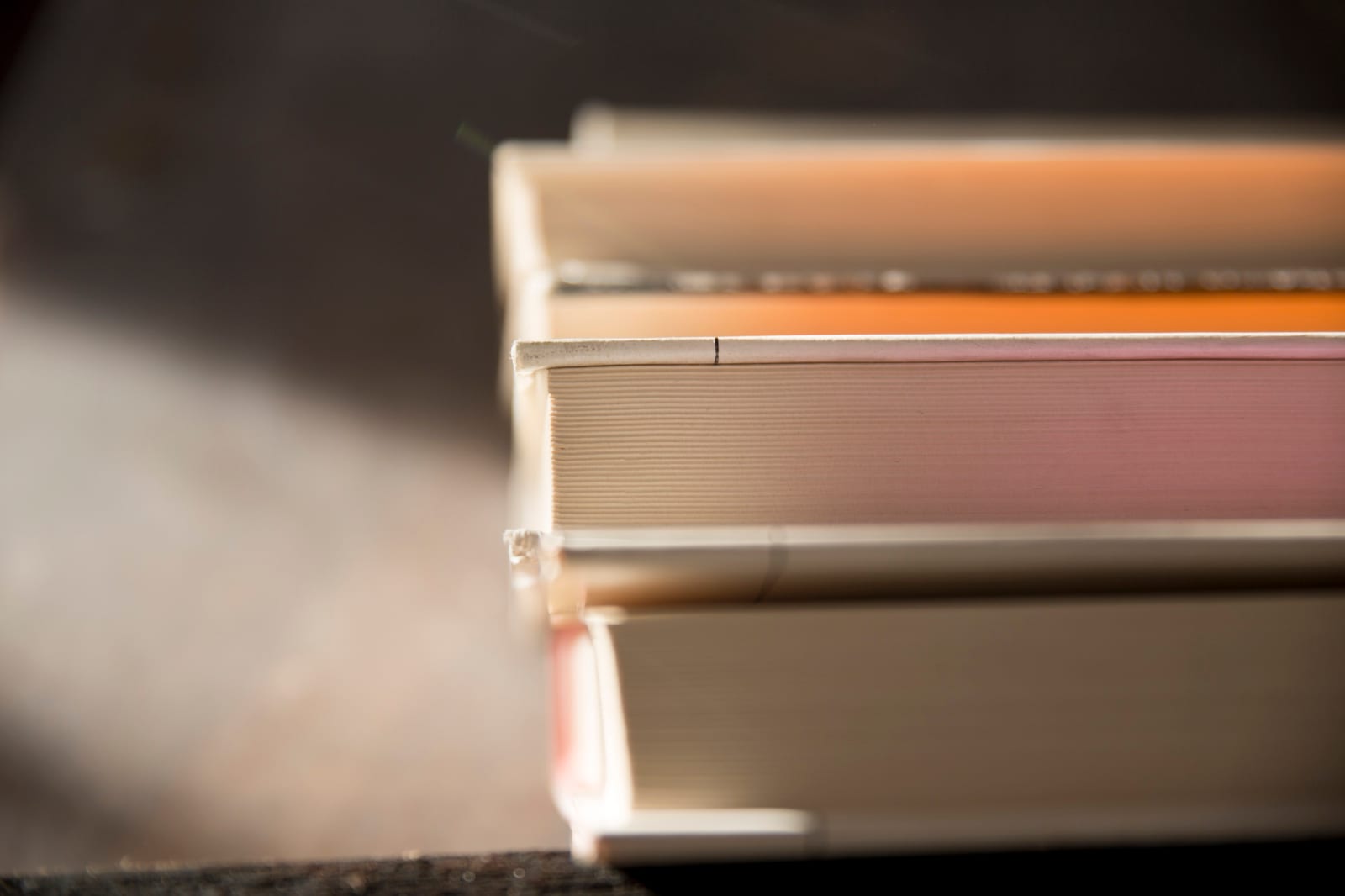 Detalhe aproximado das páginas e lombadas de vários livros empilhados, com luz lateral suave.